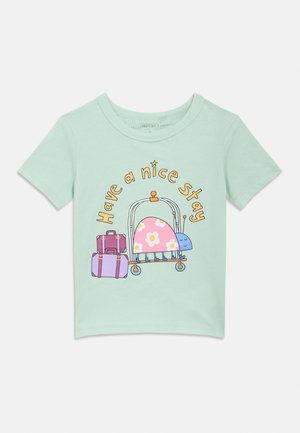 Camiseta verde menta con un gráfico divertido de un caracol en un carrito de equipaje con dos maletas moradas, rodeado por el texto "Que tengas una buena estancia".