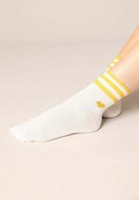Witte geribbelde sokken met gele strepen aan de bovenkant en een klein geel hartlogo. Gemaakt van katoen met een zachte textuur.