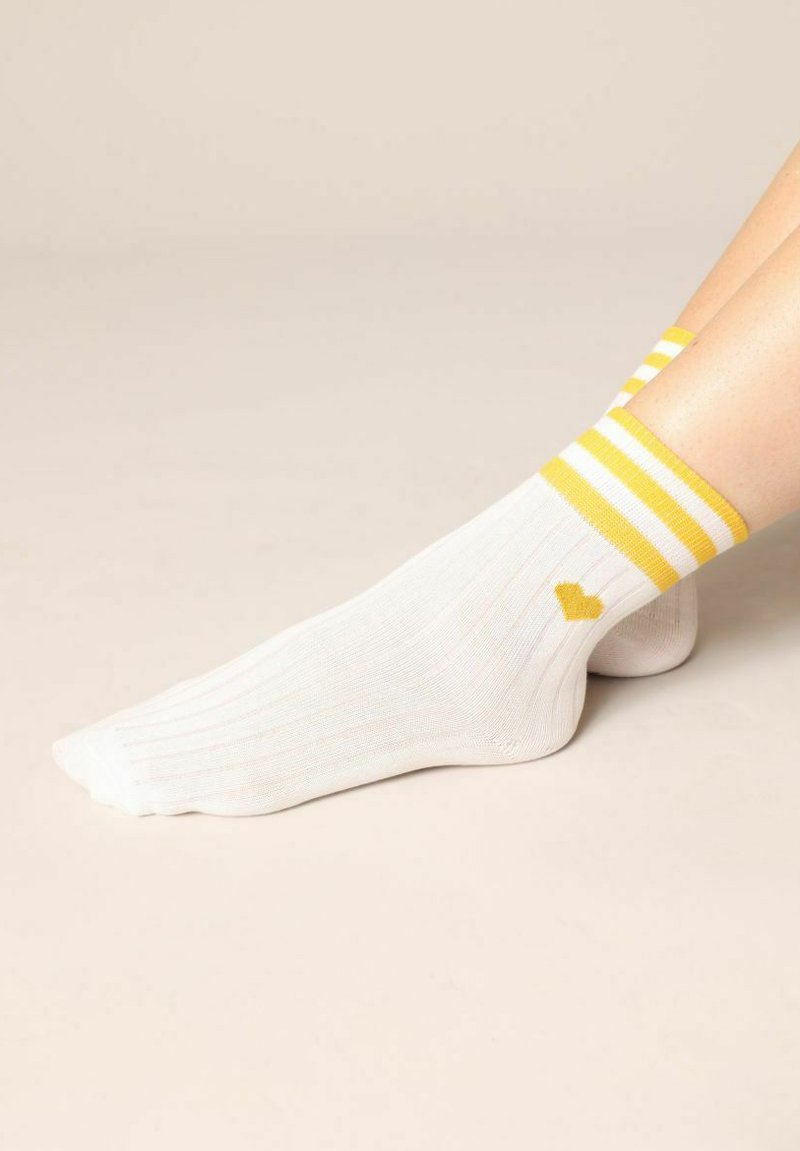Witte geribbelde sokken met gele strepen aan de bovenkant en een klein geel hartlogo. Gemaakt van katoen met een zachte textuur.