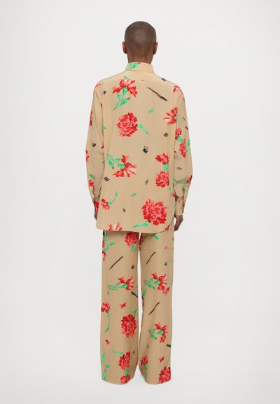 Conjunto de dos piezas floral con un fondo beige y patrones de flores rojas y verdes. Camisa de corte holgado y pantalones de pierna ancha.