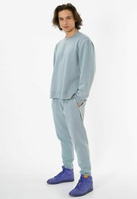 Helles blaues Sweatshirt und passende Jogginghosen aus weichem Stoff. Mit einer lässigen Passform, gerippten Bündchen und seitlichen Taschen. Getragen mit lila Turnschuhen.
