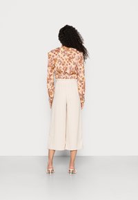Blusa floral de mangas compridas com cintura franzida, combinada com calças largas em tom creme e sandálias de salto nu. Tecido texturizado com cores de outono.