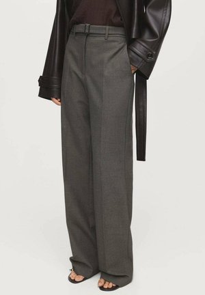 Pantalons gris à jambes larges en tissu texturé avec une ceinture, des plis à l'avant et des poches latérales ; associés à un haut sombre et une veste en cuir.