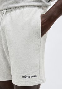 Κοντινό πλάνο ενός ατόμου που φοράει ανοιχτό γκρι σόρτς Björn Borg με το ένα χέρι στην τσέπη, δείχνοντας το λογότυπο κοντά στο τελείωμα.