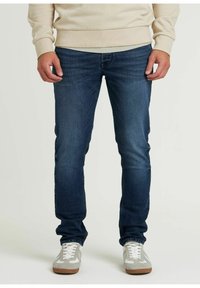 Jeans blu scuro con vestibilità slim, caratterizzati da un classico design a cinque tasche e leggere scoloriture. Indossati con sneakers grigie e bianche.