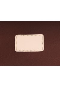 Světlý béžový obdélníkový kožený záplata s prošitím na tmavě hnědém texturovaném látkovém pozadí.