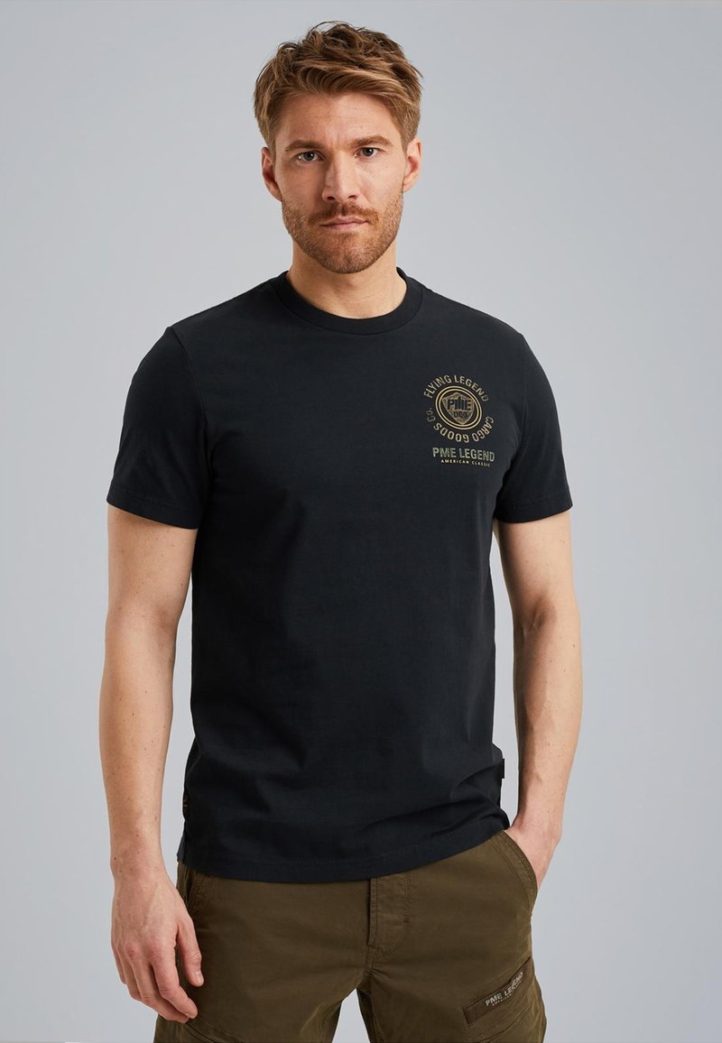 Zwarte katoenen t-shirt met korte mouwen, ronde halslijn en gouden bedrukte logo op de linkerkant van de borst. Draag het met kaki cargobroek.