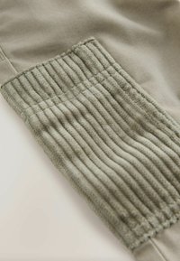 Grauer Stoff mit strukturiertem Rippdetail an einem Bündchen, mit glattem Bereich darüber. Neutrale Farbtöne und weiche Textur insgesamt.