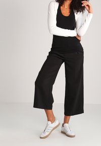 Czarne spodnie o szerokich nogawkach zestawione z dopasowanym czarnym topem i białym kardiganem z długim rękawem. Dopełnieniem stylizacji są białe trampki z beżowymi akcentami.