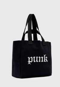 Czarna torba na ramię z filcu z czarnymi materiałowymi uchwytami, z napisem "punk" w białej gotyckiej czcionce z przodu. Prostokątny kształt.