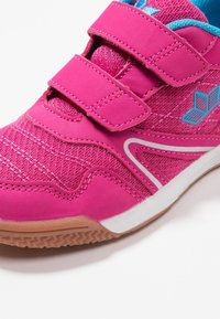 Pink athletic shoe with two Velcro straps, mesh upper, turquoise accents, and white detailing. Features a textured rubber sole for grip.