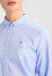 Camicia azzurro chiaro con bottoni realizzata in misto cotone. Presenta un colletto, un piccolo logo sul petto e un tessuto testurizzato.