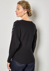 Pull noir à manches longues, orné de broderies colorées le long de la couture de l'épaule. Texture douce et coupe décontractée.