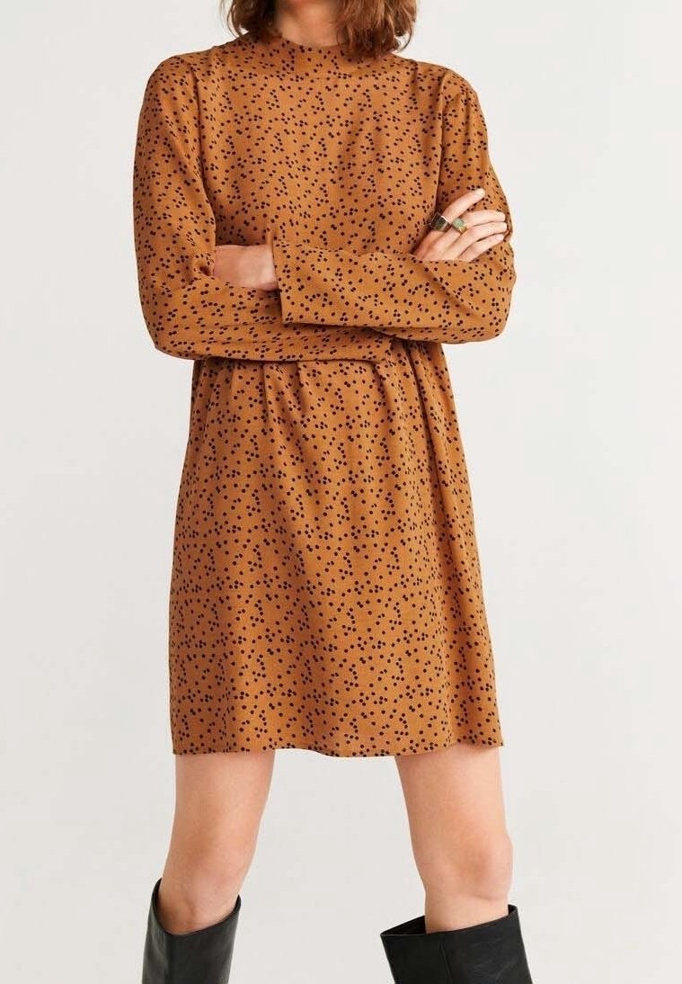 Braun Kleid mit langen Ärmeln, rundem Halsausschnitt und schwarzem Sprenkelmuster. Das Material wirkt weich; A-Linie Silhouette mit einem Taillengürtel.