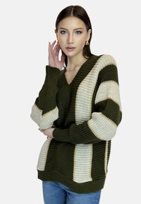 Oliven grøn og creme stribet strikket sweater med v-hals og løs pasform. Tekstureret stof med brede ærmer og ribbet kantdetalje.