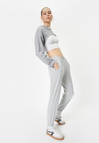 Grijze sweatshirt en joggers gemaakt van zacht materiaal; aansluitend bovenlijf met lange mouwen en elastische manchetten; witte schoenen met zwarte accenten.