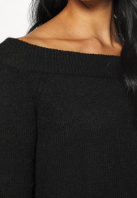 Maglione nero lavorato a maglia con design scollato, tessuto testurizzato e collo a coste, che mette in risalto un aspetto morbido e accogliente.