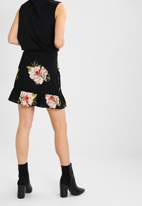 Czarna sukienka w kwiaty z rozkloszowanym dołem, z różowymi i żółtymi wzorami kwiatów. Połączona z czarnymi botkami za kostkę na masywnych obcasach.