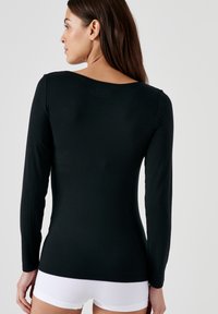 Maglietta nera a maniche lunghe con scollo ampio, realizzata in tessuto morbido, design aderente e texture liscia, abbinata a pantaloni corti bianchi.