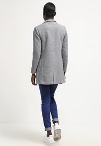 Grå ullblandning lång kappa med rak design, sidofickor och ryggslits, kombinerad med blå jeans och vita sneakers.