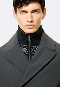 Giacca nera con colletto alto, caratterizzata da una chiusura con zip e uno strato interno trapuntato. Tessuto liscio, vestibilità su misura e design moderno.