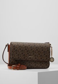 Brun DKNY crossbody-väska med monogrammönster, justerbar läderrem, guldfärgad spänne och märkesrund charm på kedja.