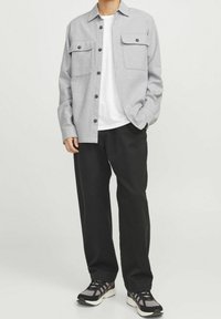 Šedá košile na knoflíky se dvěma náprsními kapsami, pod ní bílý tričko, černé pohodlné kalhoty a šedo-černé sportovní tenisky.