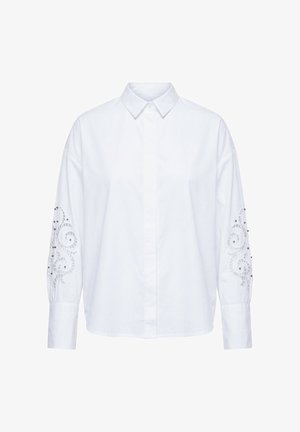 Valkoinen pitkähihaisen napillisen paitapuseron, jossa on terävä kaulus ja koristeellinen leikattu kirjailu, jossa on kierrepainatuksia ja pieniä helmiä molemmissa hihoissa.