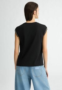 T-shirt nero a maniche corte con dettagli a catena sulle spalle. Il tessuto è liscio, con una vestibilità comoda e un delicato scollo rotondo.