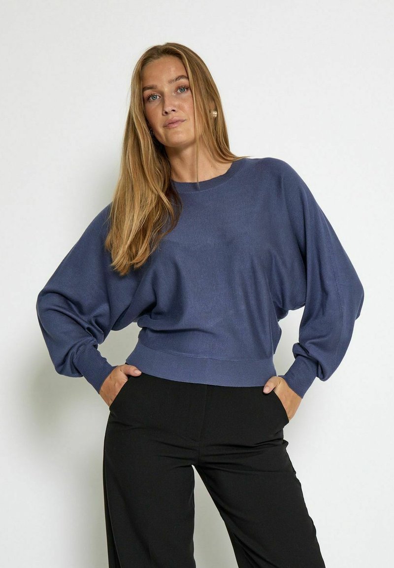 Maglione oversize blu navy con maniche a palloncino e orlo a coste, realizzato in morbido tessuto a maglia. Pantaloni neri completano l'outfit.