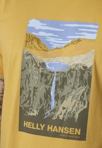 Geel katoenen t-shirt met een afgedrukte landschapontwerp met bergen, een waterval en een rivier. Onderaan staat het merk "HELIX HANSEN."