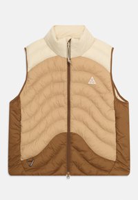 Pehmevooderiga vest kõrge kaelusega, millel on lainelised horisontaalsed tikandid beeži ja pruuni värviga. Keskel on tõmblukk ja logo detail rinnal.