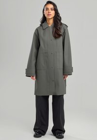 Vesikä insulationilla varustettu oliivinvihreä takki, jossa on kauluksellinen pääntie, suuret etutaskut ja napit. Tyylikäs, sileä pinta ja rento istuvuus.