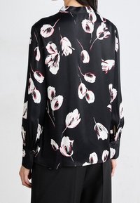 Blouse en satin noir avec un motif floral blanc et rouge, manches longues avec poignets boutonnés et un col classique.