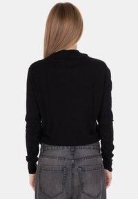 Maglione nero lavorato a maglia con maniche lunghe, scollo rotondo e polsini a coste, abbinato a jeans grigi a vita alta. Finitura texturizzata visibile.