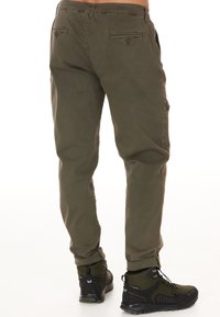 Olivgröna cargobyxor med rak passform, med sidofickor och en knappficka bak, tillsammans med svarta vandringskängor.