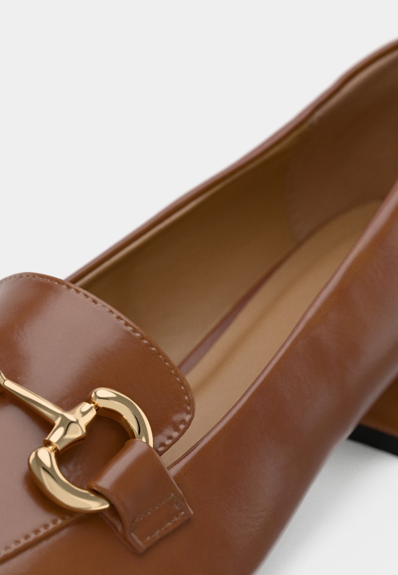 Mocassins en cuir verni marron avec un accent en métal doré. Ils disposent d'une finition lisse et d'un design à bout rond.