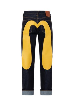 Jeans in denim blu scuro con risvolti e un grande motivo giallo sul retro che ricorda gli archi di McDonald’s.