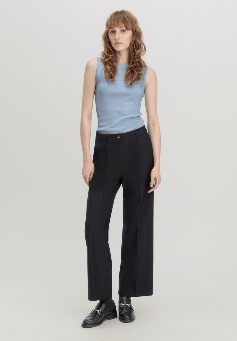 Lichtblauw mouwloos topje, hoog- taille zwarte wijde broek en zwarte schoenen met gouden accenten. Gladde texturen en een perfect pasvorm.