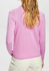 Pitkähihainen neulepusero pehmeästä vaaleanpunaisesta neuloskankaasta. Siinä on resorit helman ja hihansuiden kohdalla, pyöreä pääntie ja vartalonmyötäinen siluetti.