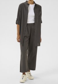Chemise grise à boutons avec manches retroussées, associée à un pantalon élastiqué gris et des baskets crème avec des détails contrastés. Texture lisse.