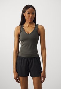 Athletic tank top i mørkegrønn med v-hals og slank passform, kombinert med svarte shorts med elastisk midjebånd og sidelommer.