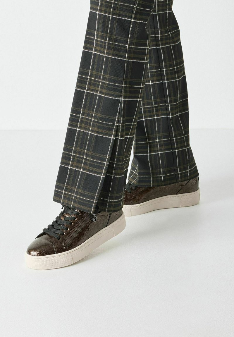 Sneakers in pelle marrone con finitura testurizzata e lacci grigi, abbinati a pantaloni a quadri neri con linee bianche e gialle.