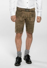 Pantalones cortos de lederhosen de ante marrón con costuras decorativas, botones laterales y un cinturón a juego con una hebilla grabada. Llevados con calcetas grises hasta la rodilla.