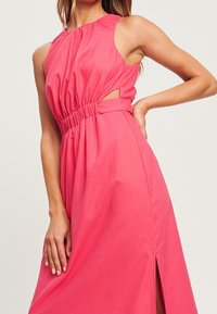 Robe sans manches rose avec un ruché à la taille, des découpes sur les côtés et une fente haute sur la cuisse pour plus de texture et de silhouette.