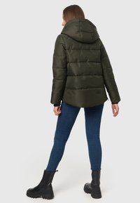 Dark green puffer jacket with a detachable hood, horizontal quilted pattern, and black accents. Paired with blue jeans and black ankle boots.
