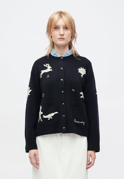 Black knit cardigan featuring cream embroidered animal and nature motifs, with a buttoned front and two front pockets. Text "harmony" included.