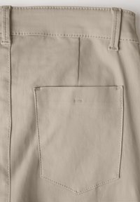 Beige stof met een gladde textuur, voorzien van een enkele achterzak en tonale stiksels, benadrukt een schoon en eenvoudig ontwerp.