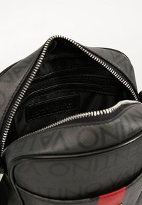 Black leather bag with zip closure, featuring an interior pocket, logo detailing, and a bold red accent. Textured surface with subtle patterns.