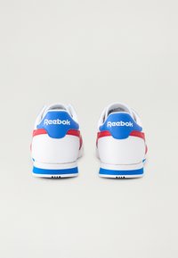Balti sportbačiai su raudonais ir mėlynais akcentais, turintys lygų viršutinį sluoksnį, paminkštintą padas ir mėlyną kulno juostelę su "Reebok" logotipu.